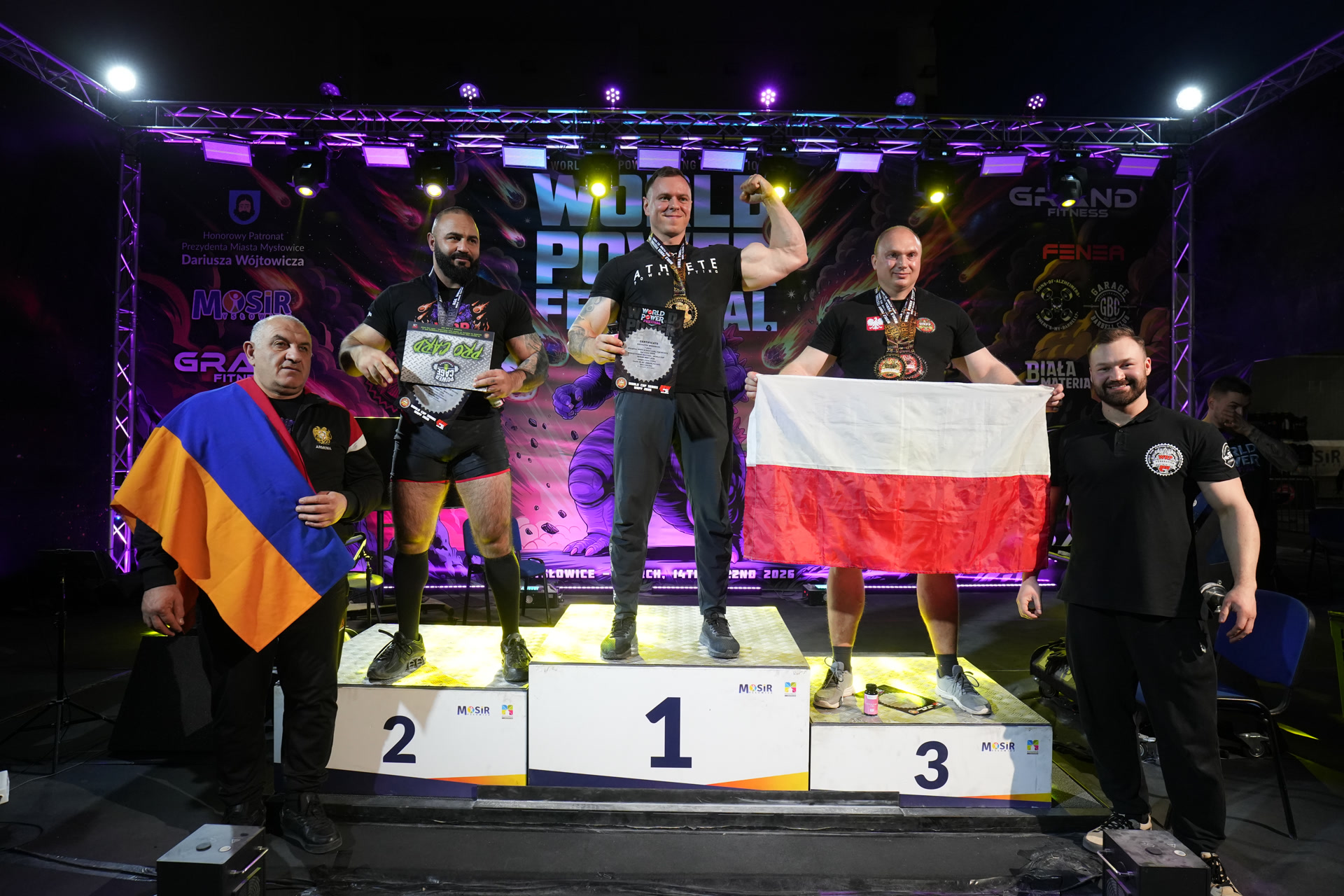 Krzysztof Wierzbicki na najwyższym stopniu podium World Power Festival, z flagą Polski w tle